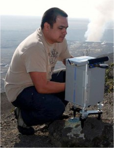 usgs-gravity_collection An HVO scientist measures gravity at a station on the rim of Kilauea caldera. The plume from the summit eruption in Halema`uma`u Crater can be seen in the background. Photo courtesy of USGS/HVO