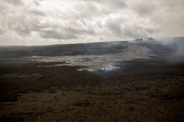 The lava flow fed the northeastern lava lake in Puʻu ʻŌʻō remains weakly active at the northern base of the Puʻu ʻŌʻō cone. The front of the flow is burning lichen on old ʻAʻā flows erupted from Puʻu ʻŌʻō during 1983–1986. The eastern edge of Puʻu ʻŌʻō is at the upper right side of the photo. Photo courtesy of USGS/HVO