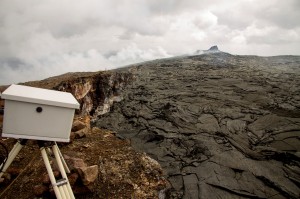 The eastern rim of Puʻu ʻŌʻō is no longer visible, having been buried by flows mostly from the small lava lake on the northeast side of the crater floor. A mound of lava with a complex of spatter cones, visible in the background, now surrounds the lava lake, which is only visible from the air. Lava from the lava lake is feeding a small lava flow active at the northern base of the Puʻu ʻŌʻō cone. The box in the foreground houses the Puʻu ʻŌʻō Crater webcam shown on the HVO webpage. A time-lapse camera on a tripod is visible on the crater rim in the distance. Photo courtesy of USGS/HVO
