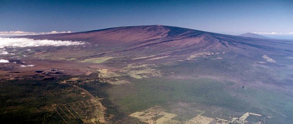 USGS Hawaiian Volcano Observatory scientists are closely monitoring recent signs of unrest on Mauna Loa, the largest active volcano on Earth. In this 1985 aerial photo, Mauna Loa looms above Kīlauea Volcano’s summit caldera (left center) and nearly obscures Hualālai in the far distance (upper right). USGS photo.