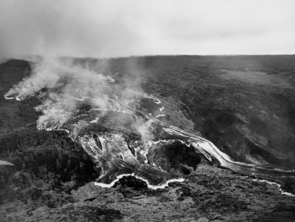 This rapidly moving ʻaʻā lava flow was one of several that advanced down the west flank of Mauna Loa during the volcano’s 1950 eruption. The massive flow, tens of meters (yards) high, traveled from the Southwest Rift Zone vent to the ocean, a distance of about 18 km (11 mi), in around 18 hours. Two earlier flows from this eruption reached the ocean in as little as three hours. All three flows crossed Highway 11 as they advanced to the sea. In this black-and-white aerial photo, incandescently hot areas on the flow appear white. Photo credit: Air National Guard, 199th Fighter Squadron.
