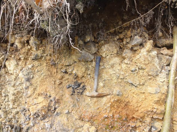The dark-colored charcoal (left of rock hammer) from a log buried by lava was found at the base of an ‘ā‘a flow in the District of Ka'ū on the Island of Hawaiʻi. The age of this charcoal, determined by an accelerator mass spectrometer radiocarbon method, is 2075 plus or minus 36 years before present. USGS photo.