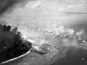 The first wave of LVT(A)s move toward the invasion beaches, passing through the inshore bombardment line of LCI gunboats, 15 September 1944. Cruisers and battleships are bombarding from the distance. The landing area is hidden bu dust and smoke. Photographed from a USS Honolulu (CL-48) plane. Source: NARA 80-G-283533.