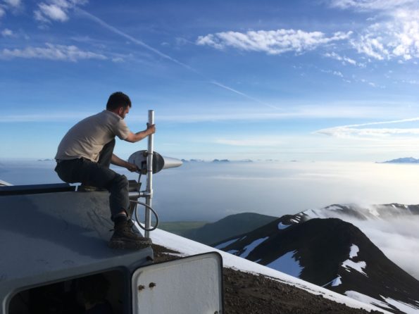 A USGS Hawaiian Volcano Observatory scientist, while assisting Alaska Volcano Observatory colleagues this summer, mounted a radio antenna on an upgraded seismic station at Great Sitkin Volcano in the western Aleutian Islands. USGS photo by A. Darold, 06-20-2019.