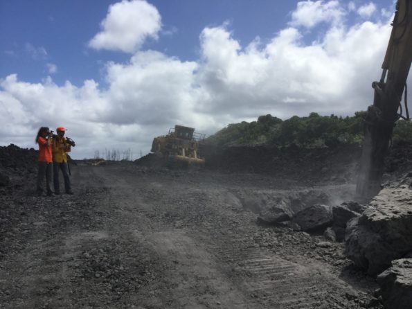 Two HVO geologists document road cutting activities on HWY 132 on August 7, 2019. One geologist is taking visual photographs while another geologist is taking thermal photographs to make a tandem pair for comparison. The temperature of the solidified lava was measured to 425° C (800° F) at the digging site. Photograph by USGS geologist K. Mulliken.